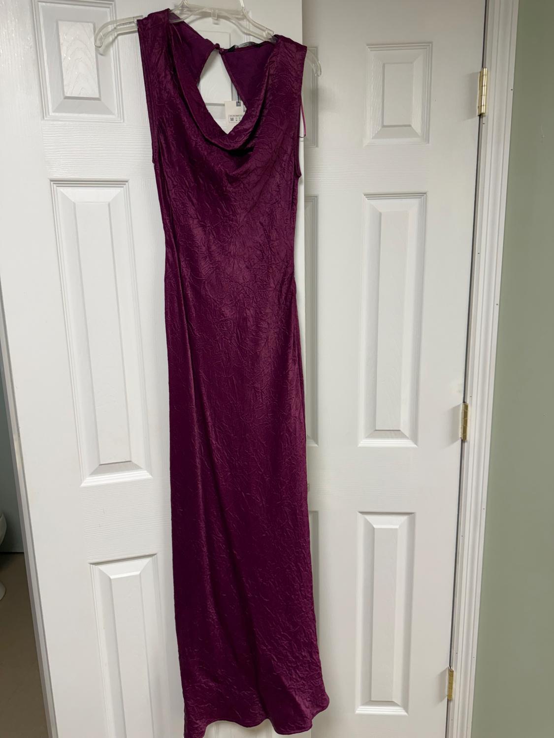 Long purple dress with a crinkled texture, hanging on a clear hanger over a white door.