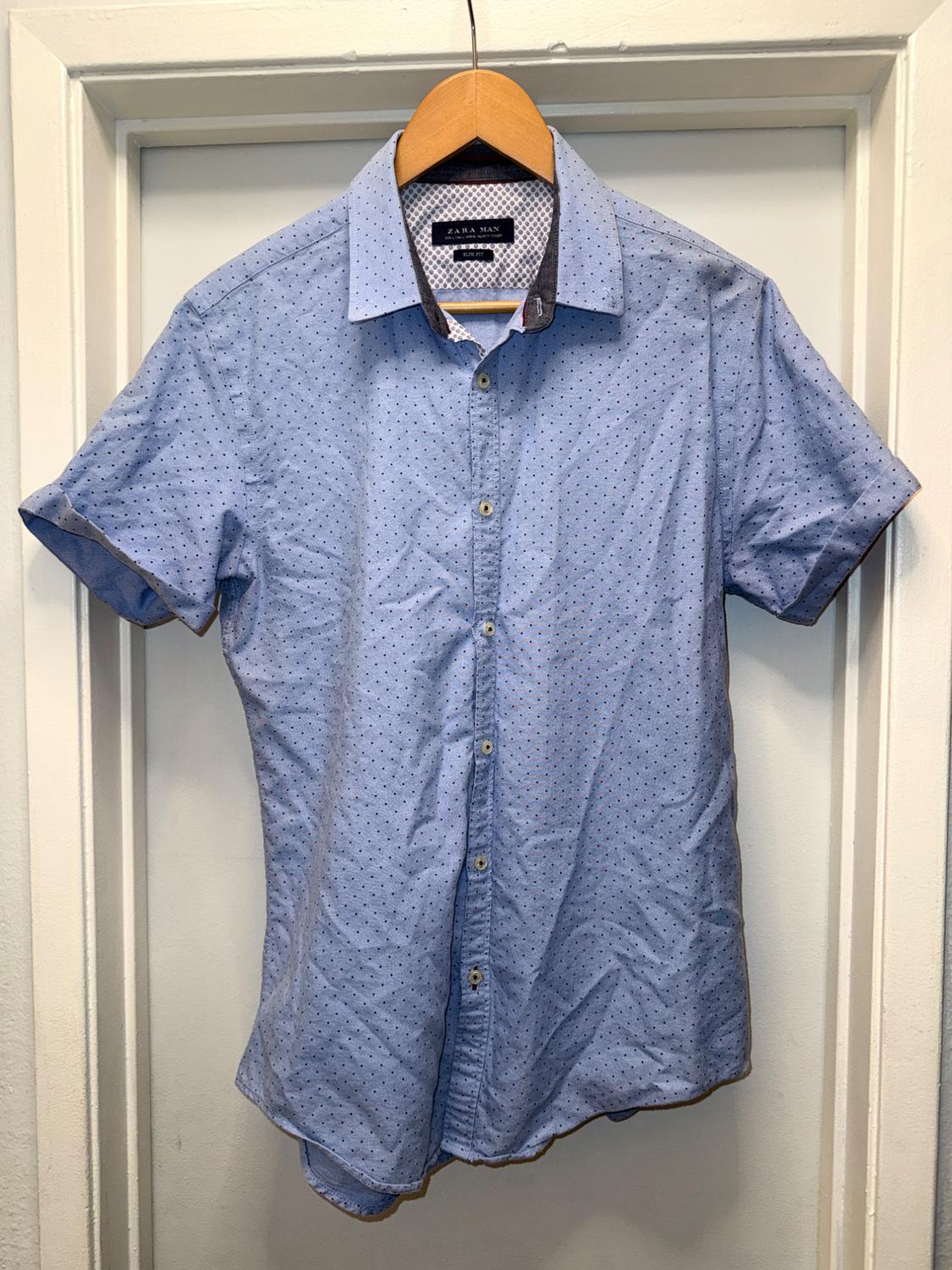 Light blue short-sleeve shirt with small dark dots on a wooden hanger on a white door. Text: ZARA MAN SLIM FIT.