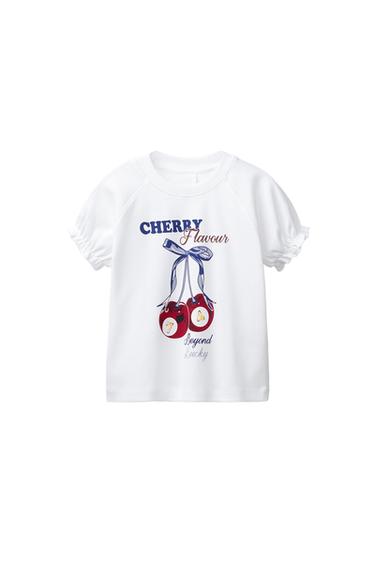 Front view of a white T-shirt with a cherry print and the text "Cherry Flavour Beyond Lucky". Short sleeves with frill detail.
