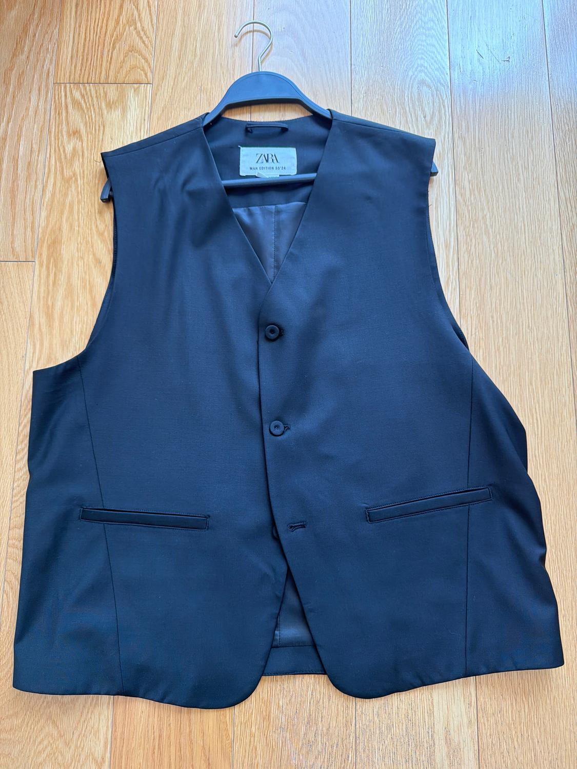 Black dress vest hanging on a hanger over a light wood floor. Visible tag: "ZARA MAN EDITION".