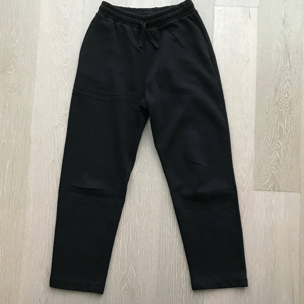 Black track pants with an elastic waistband and an adjustable drawstring, placed on a light wooden floor.