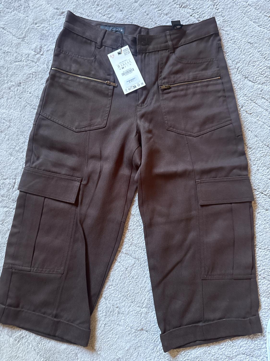 Brown cargo trousers with pockets and zips, visible hang tag, on a light background.