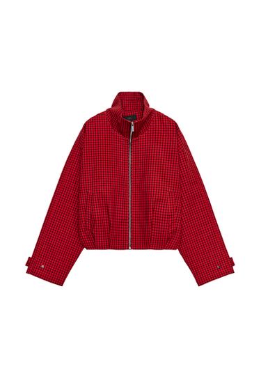 Front view of red jacket with black checks. Funnel neck, long sleeves with tab detail, central zip fastening and side pockets.