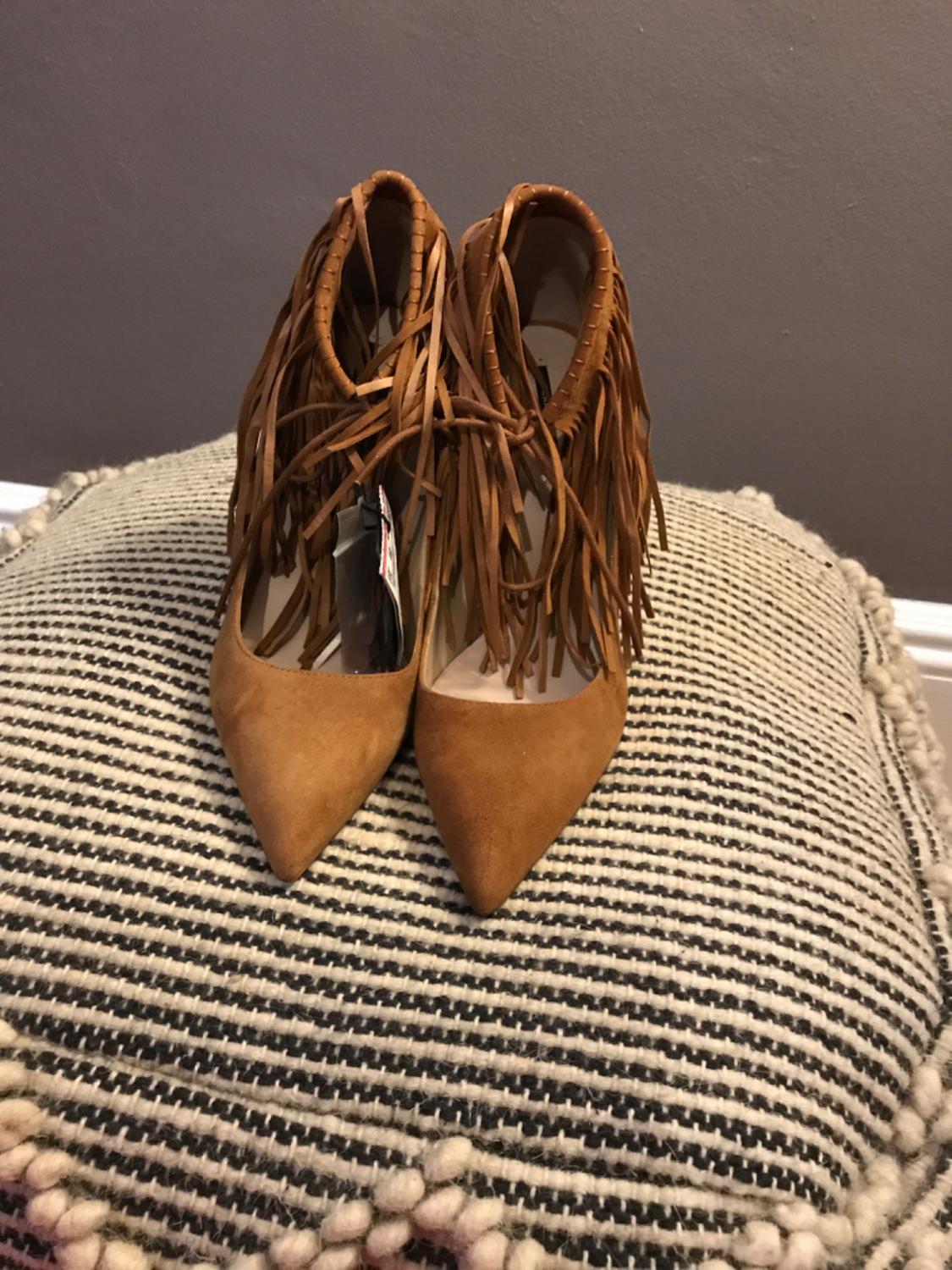 Brown fringed shoes, pointed toe, on a striped cushion.