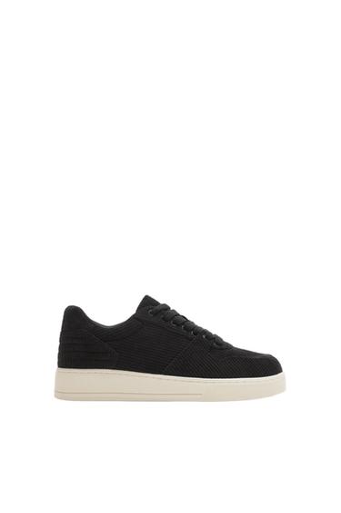 Side view of a black trainer with a white sole and laces.