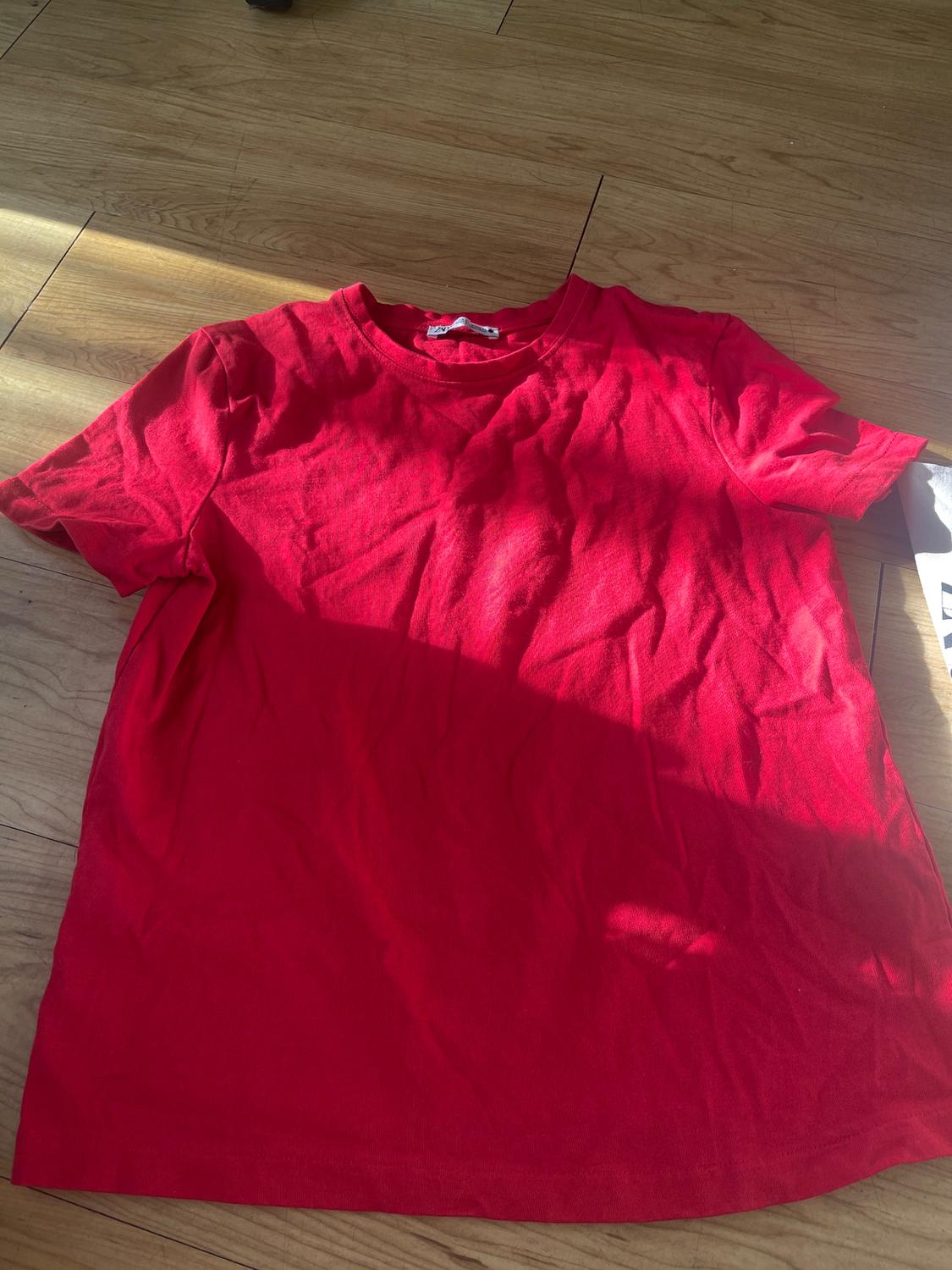 Red short-sleeved t-shirt on a wooden floor, illuminated by sunlight.