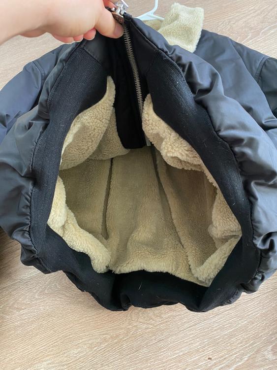 Black jacket with a beige lining interior, open to show the soft material. Hand holding the zipper against a wooden background.