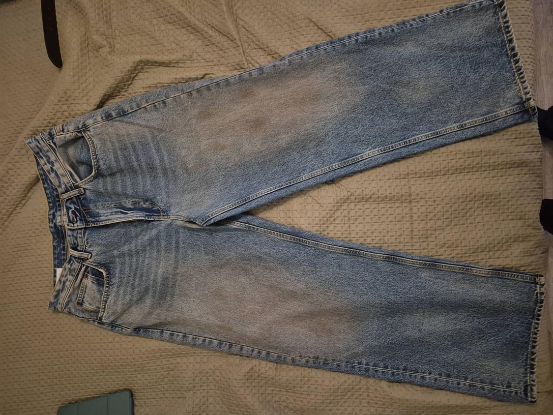 Light blue wide-leg jeans with a distressed effect, laid out on a textured beige fabric in a relaxed style composition.