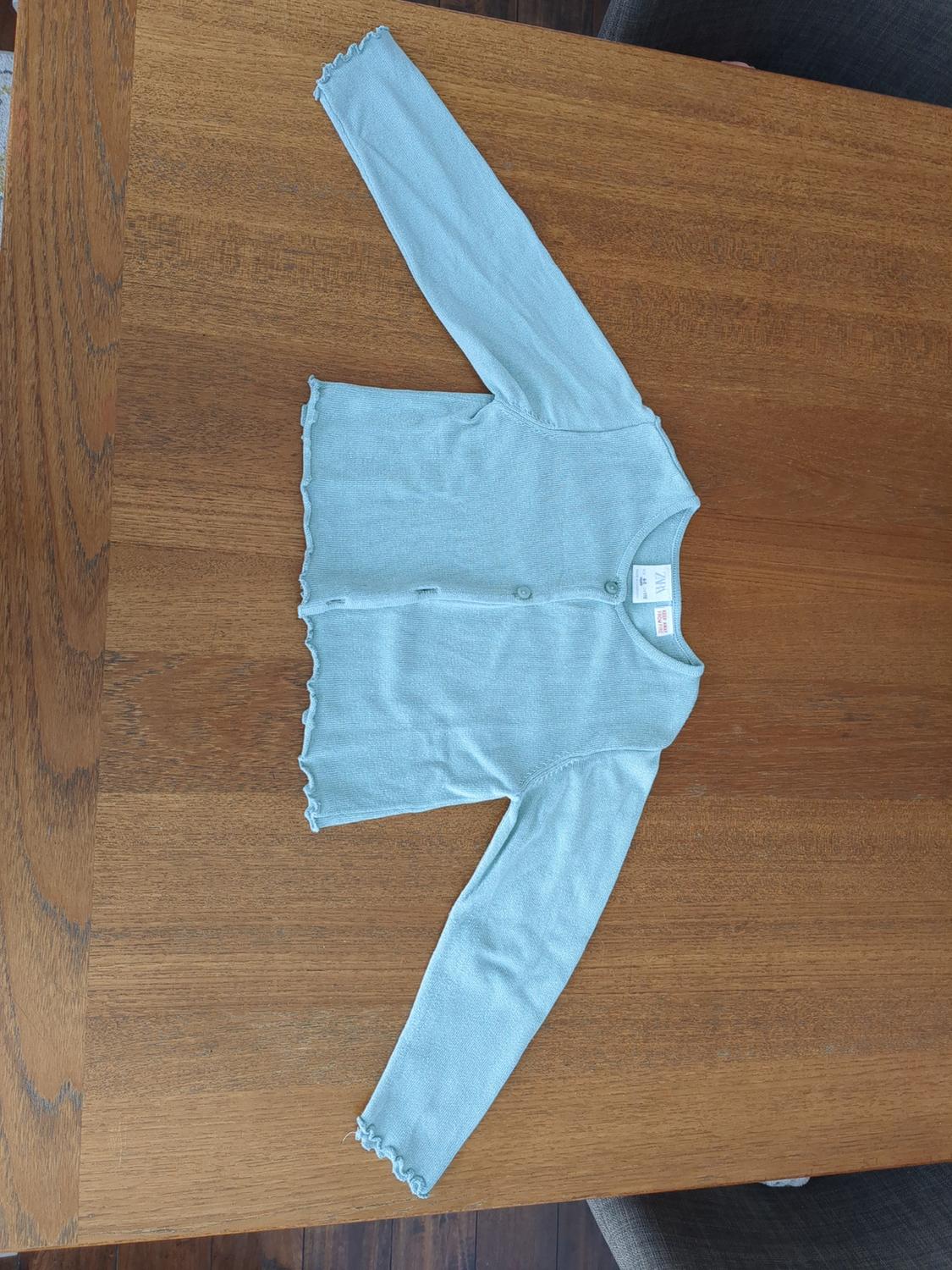 Light blue long-sleeved cardigan with buttons, placed on a wooden table.