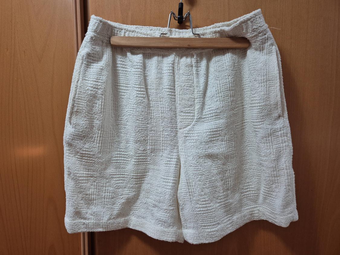 White textured fabric shorts hanging on a wooden hanger over a light wooden door.