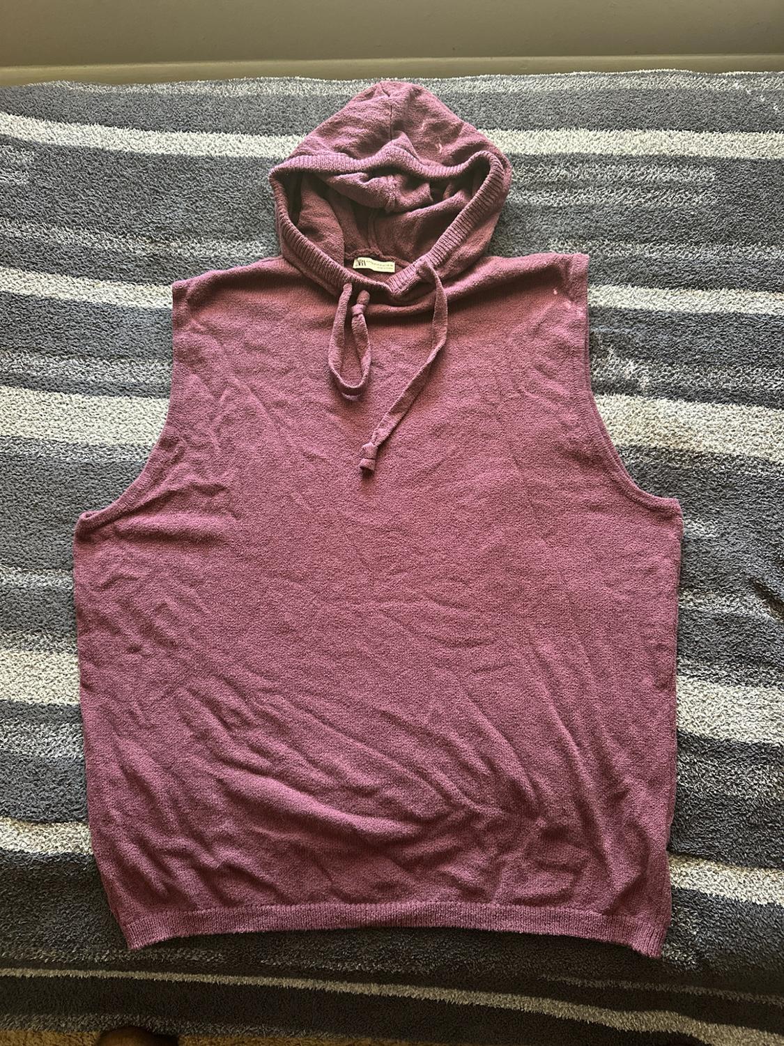 Sleeveless knit hoodie with a hood and drawstrings in a mauve tone, spread out over a gray-and-white striped blanket.