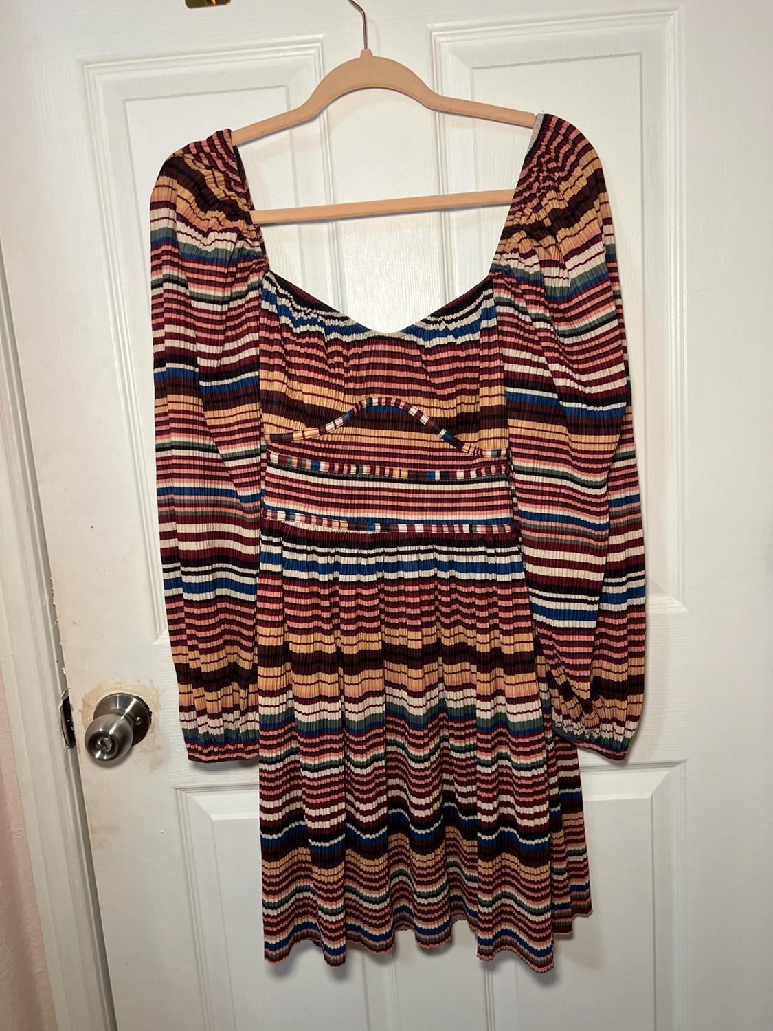 Long-sleeved dress with a ribbed texture and multicoloured stripes, hanging on a wooden hanger against a white door.