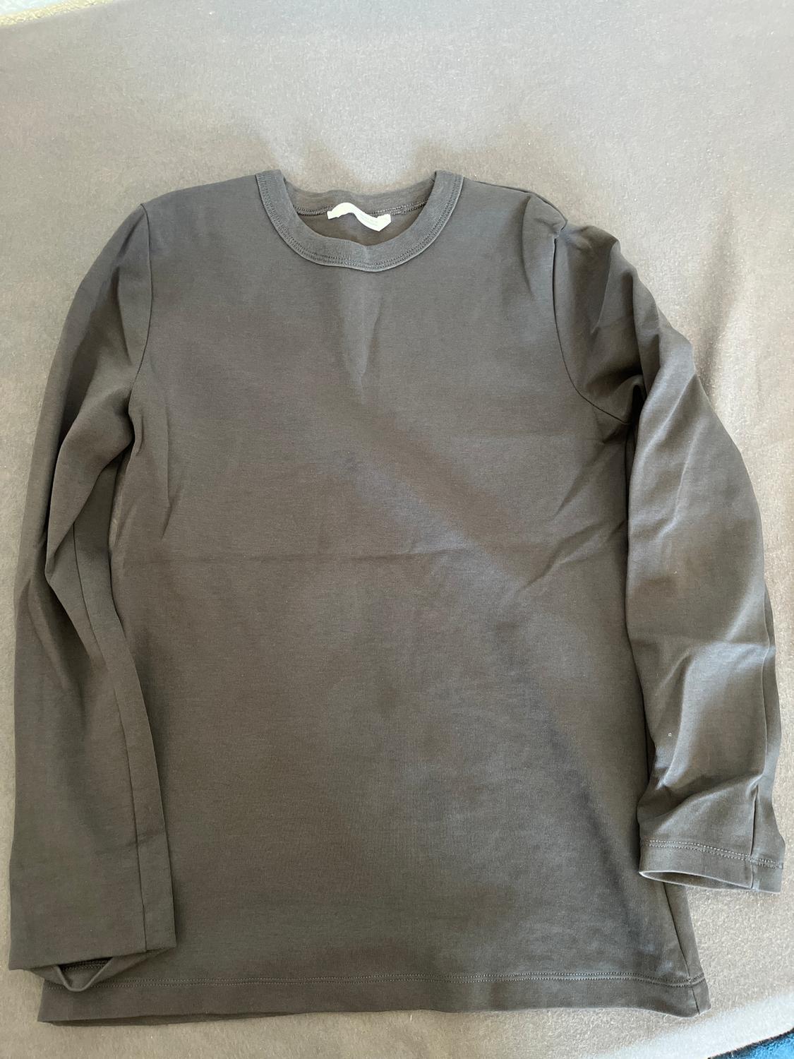 Dark grey long-sleeved T-shirt on a light grey surface. The garment is laid out flat and slightly wrinkled.