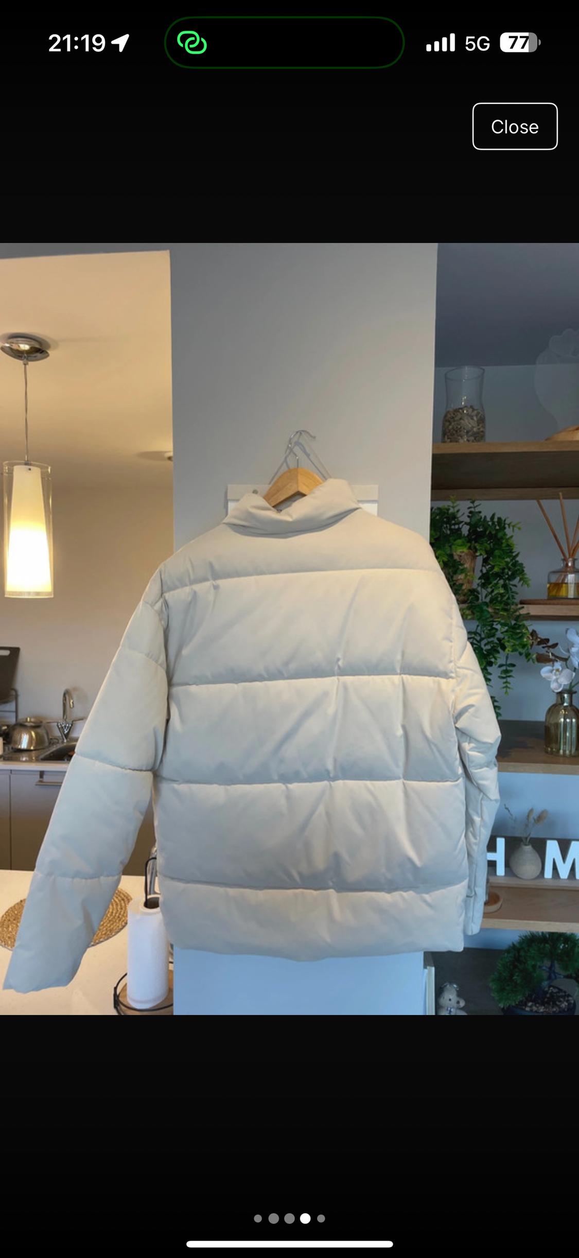Beige padded jacket hanging on a hanger inside a modern kitchen with warm lighting and decorative shelves.