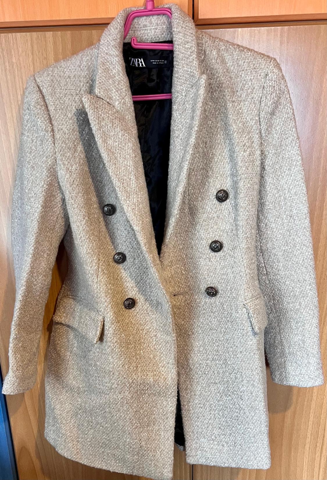 Grey double-breasted wool coat with wide lapels, hanging on a pink hanger. Visible label on the inside.