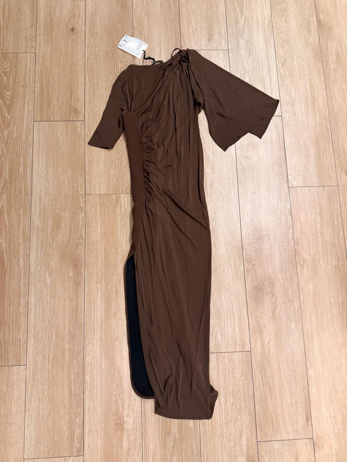 Brown asymmetric long dress with short sleeves, ruching and a side slit, laid out on a wooden floor.