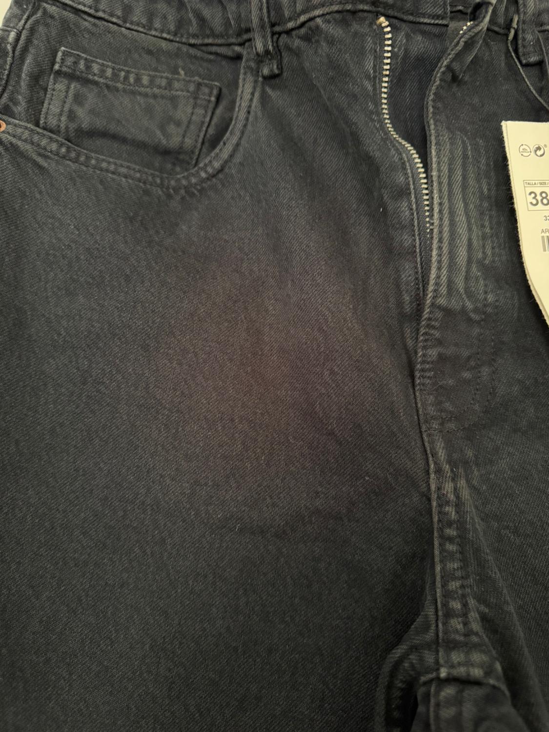 Detail of black jeans with the zip undone and front pocket. Visible label with the text TALLA / SIZE 38.