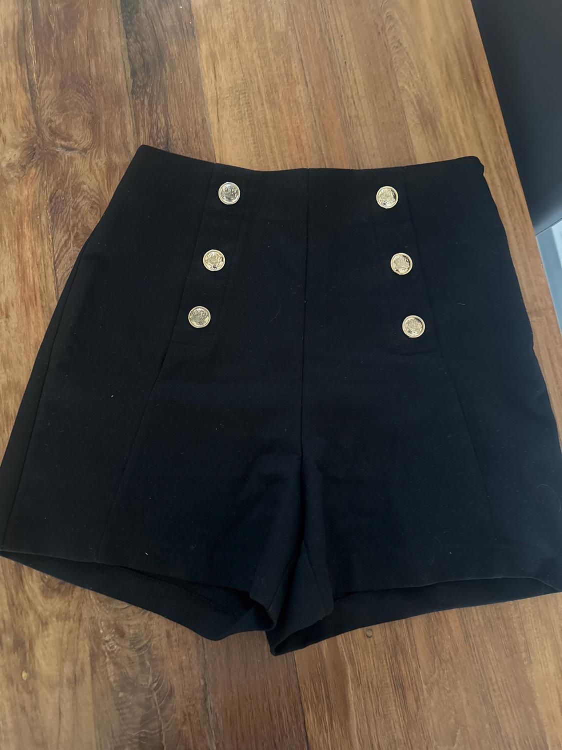 Black shorts with six gold buttons on the front, on a wooden table.