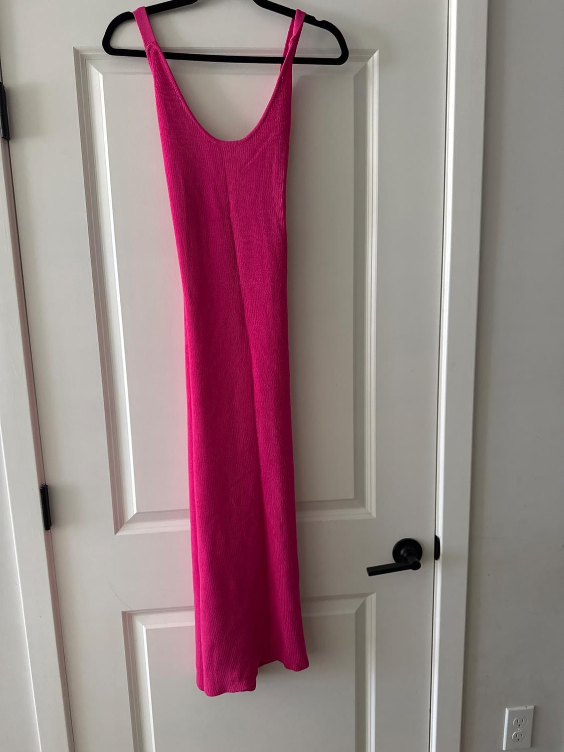 Fuchsia pink maxi dress hanging on a black coat hanger on a white door with a black handle.