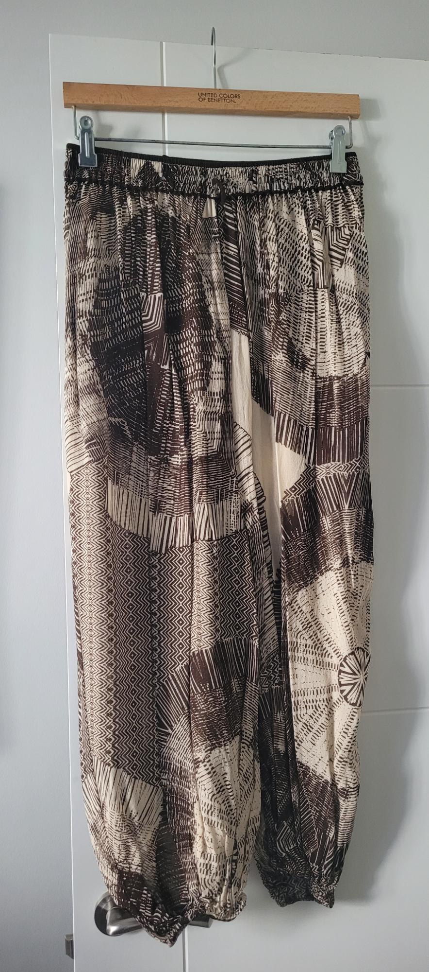 Loose-fitting trousers with a geometric print in brown and beige tones, hanging on a wooden hanger from United Colors of Benetton.