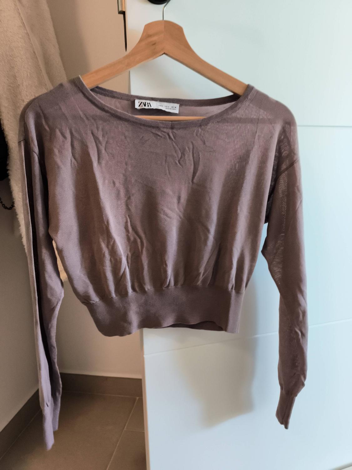 Creased brown jumper hanging on a wooden hanger, with a visible tag, against a white wardrobe and beige wall.