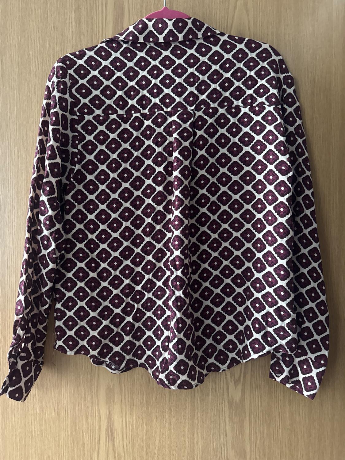 Rear view of a maroon and white geometric print long-sleeve shirt, hanging on a pink hanger against a wooden background.