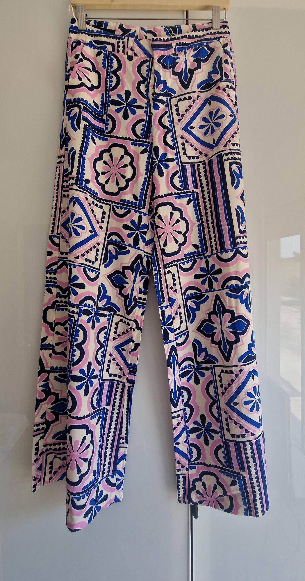 Trousers hanging on a hanger with a geometric and floral print in shades of blue, pink and white on a light background.