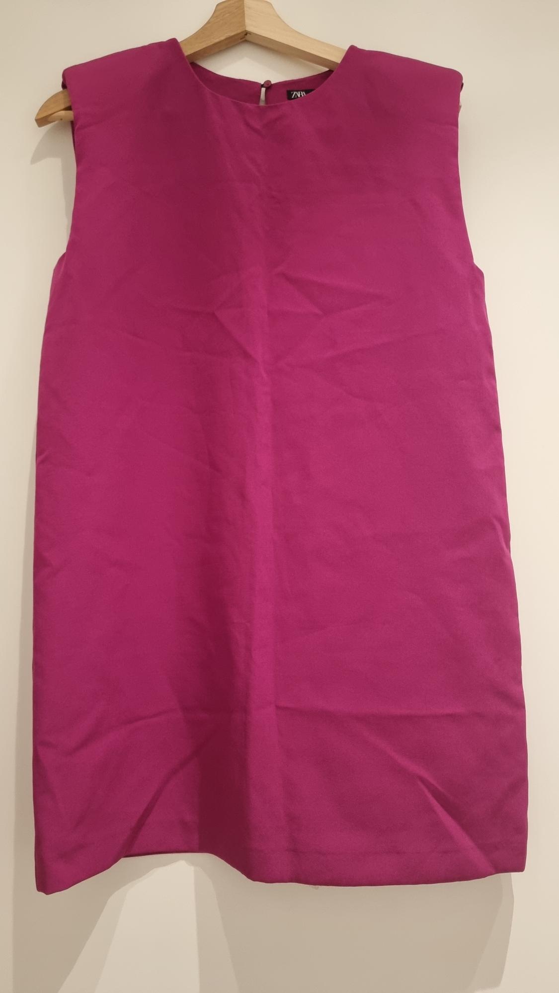 Fuchsia sleeveless dress hanging on a wooden hanger, white background. Label visible on the collar.