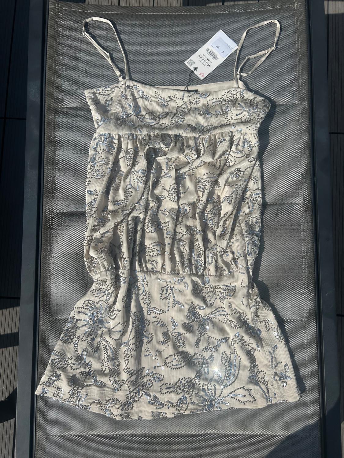 Beige strappy top with silver floral sequins and a ruched waist, laid out on an outdoor chair in the sunlight.