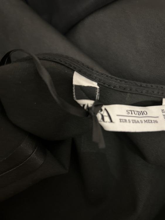 Black fabric clothing label that reads "STUDIO EUR S USA S MEX 26". Dark background and visible soft texture.