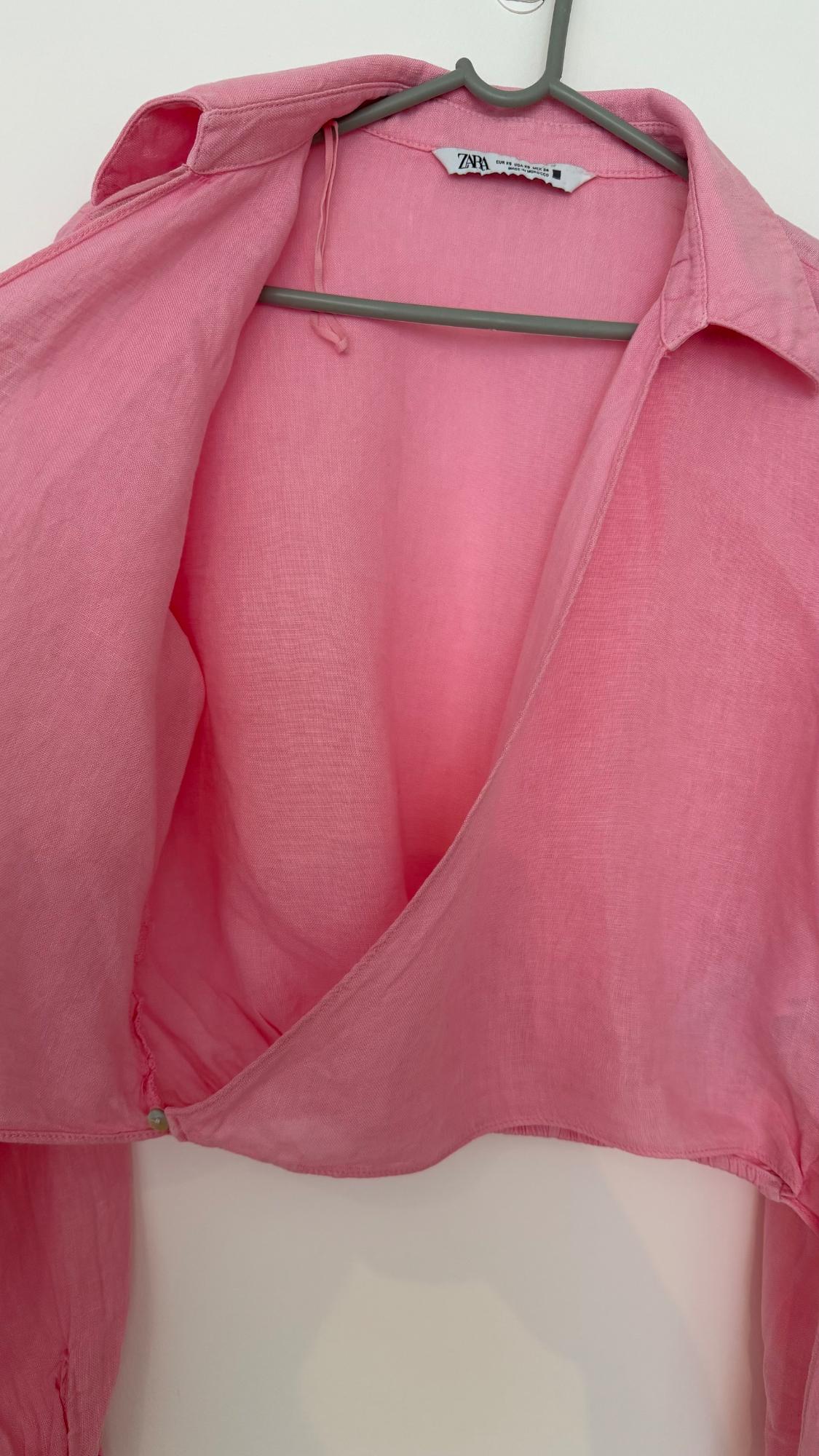 Pink crossover shirt hanging on a hanger against a white background. Visible label with the text ZARA EUR XS USA XS MEX 24 MADE IN MOROCCO.