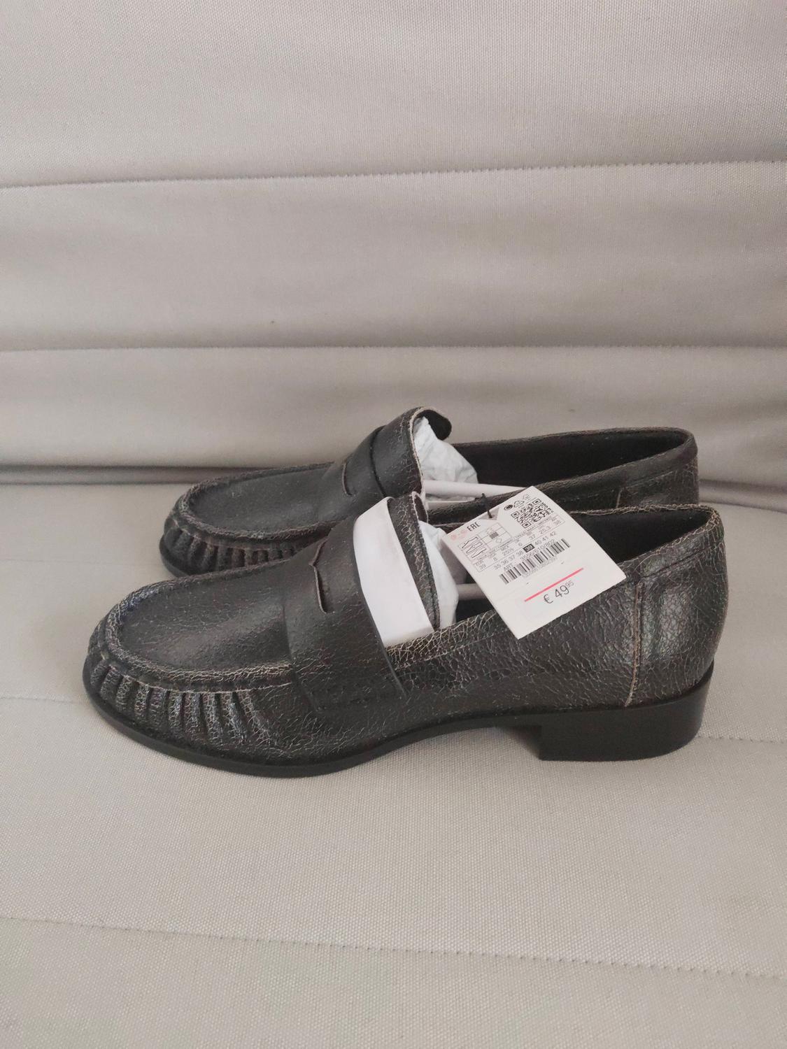 Black leather shoes with a €49 price tag on a light grey background. Classic design with visible stitching.
