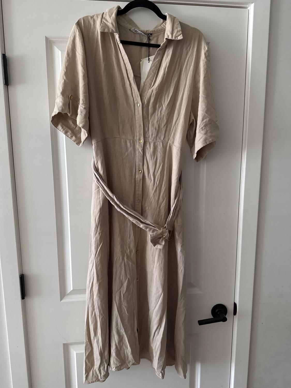 Beige short-sleeved dress with belt, hanging on a black hanger over a white door.