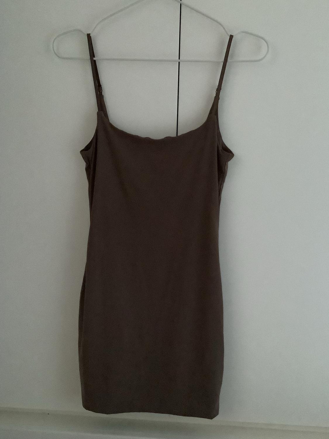 Dark brown, tight-fitting, spaghetti strap mini dress, hanging on a hanger against a white wardrobe. Minimalist and relaxed style.