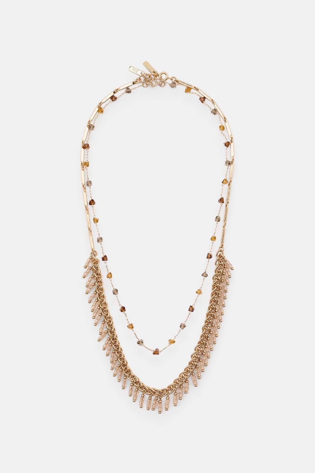 Front view of two layered gold necklaces. One thin with dark beads and another thicker chain with multiple dangling beads.