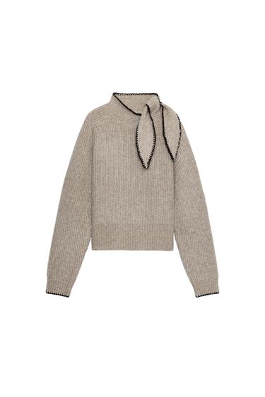 Front view of a taupe jumper with a high neck and bow. Contrast stitching and long sleeves.