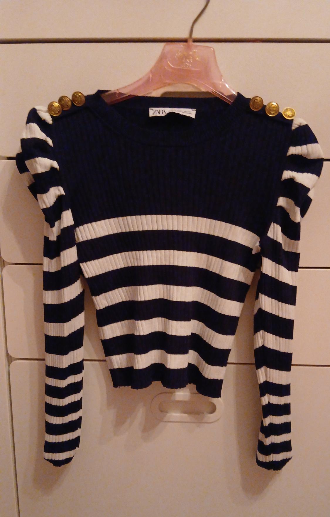 Navy and white striped jumper with gold buttons on the shoulders, hanging on a clear pink hanger.