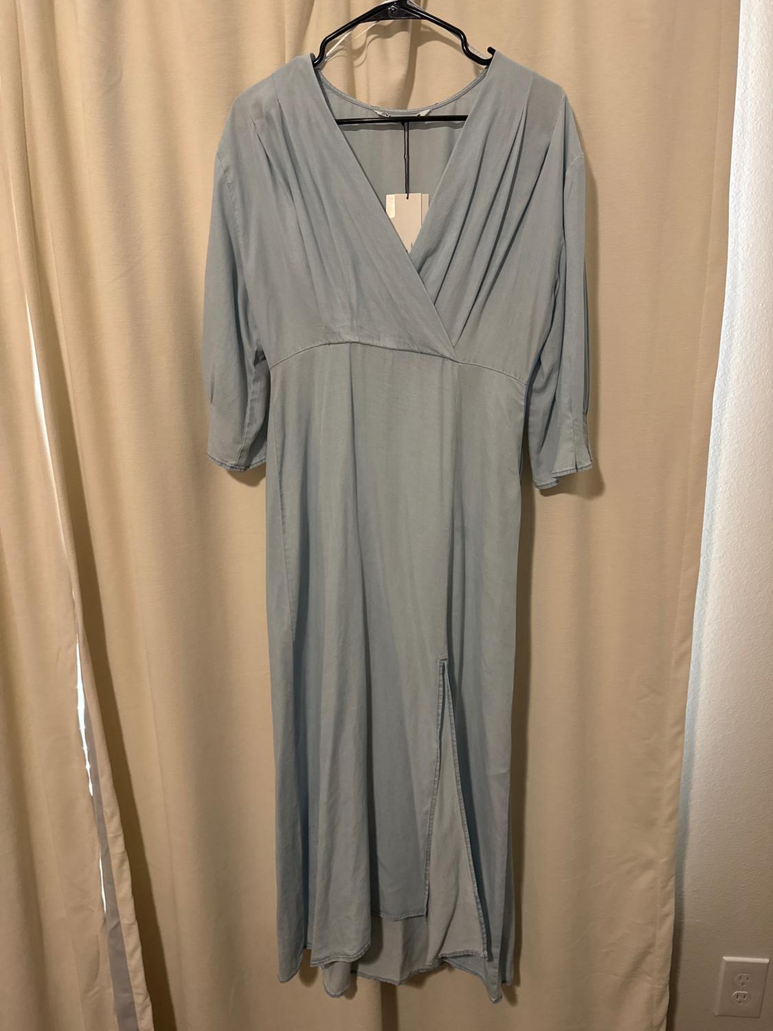 Light blue three-quarter sleeve dress hanging on a black hanger in front of a beige curtain.
