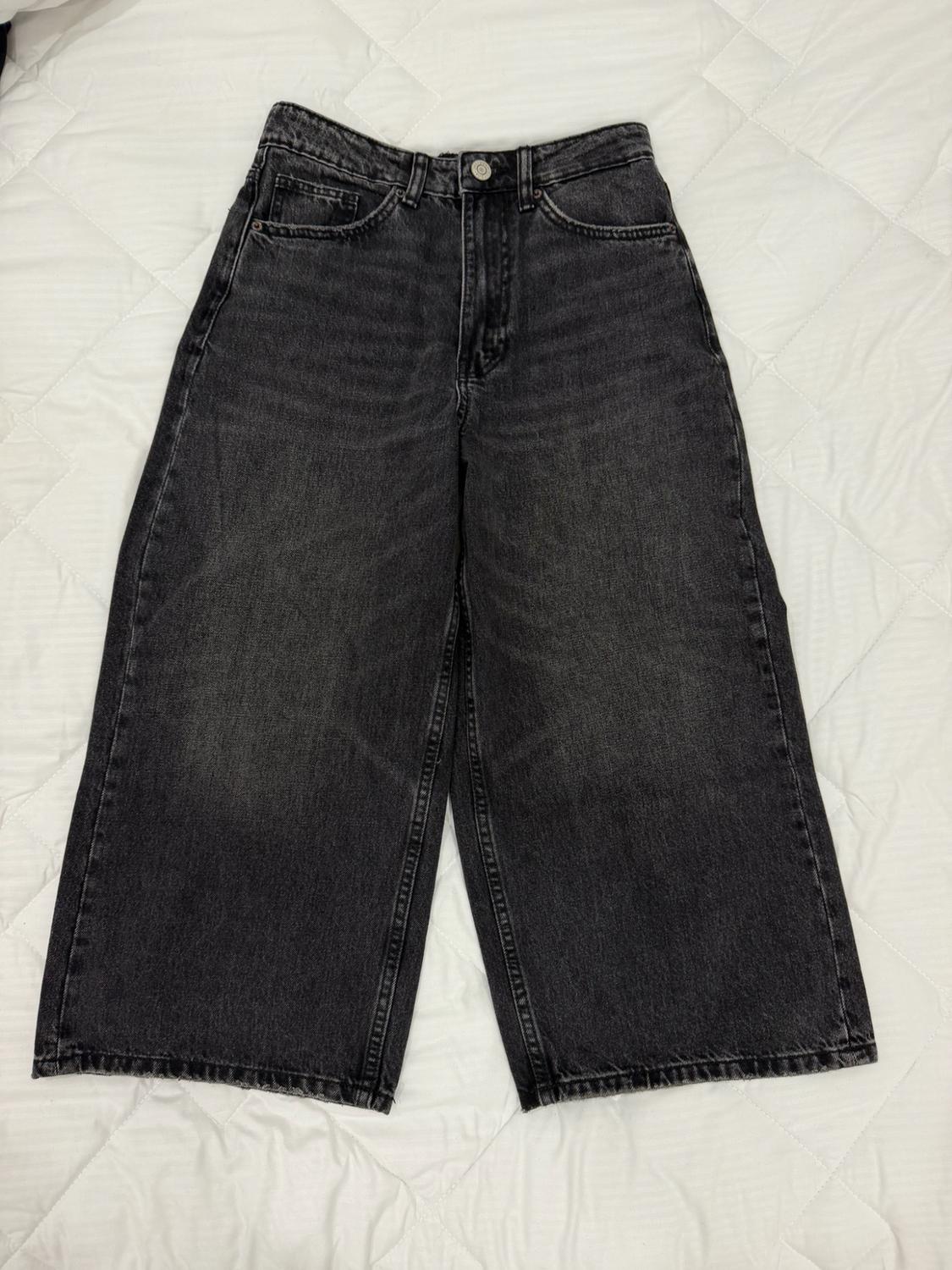 Black, high-waisted, wide-leg jeans laid out on a padded white surface.