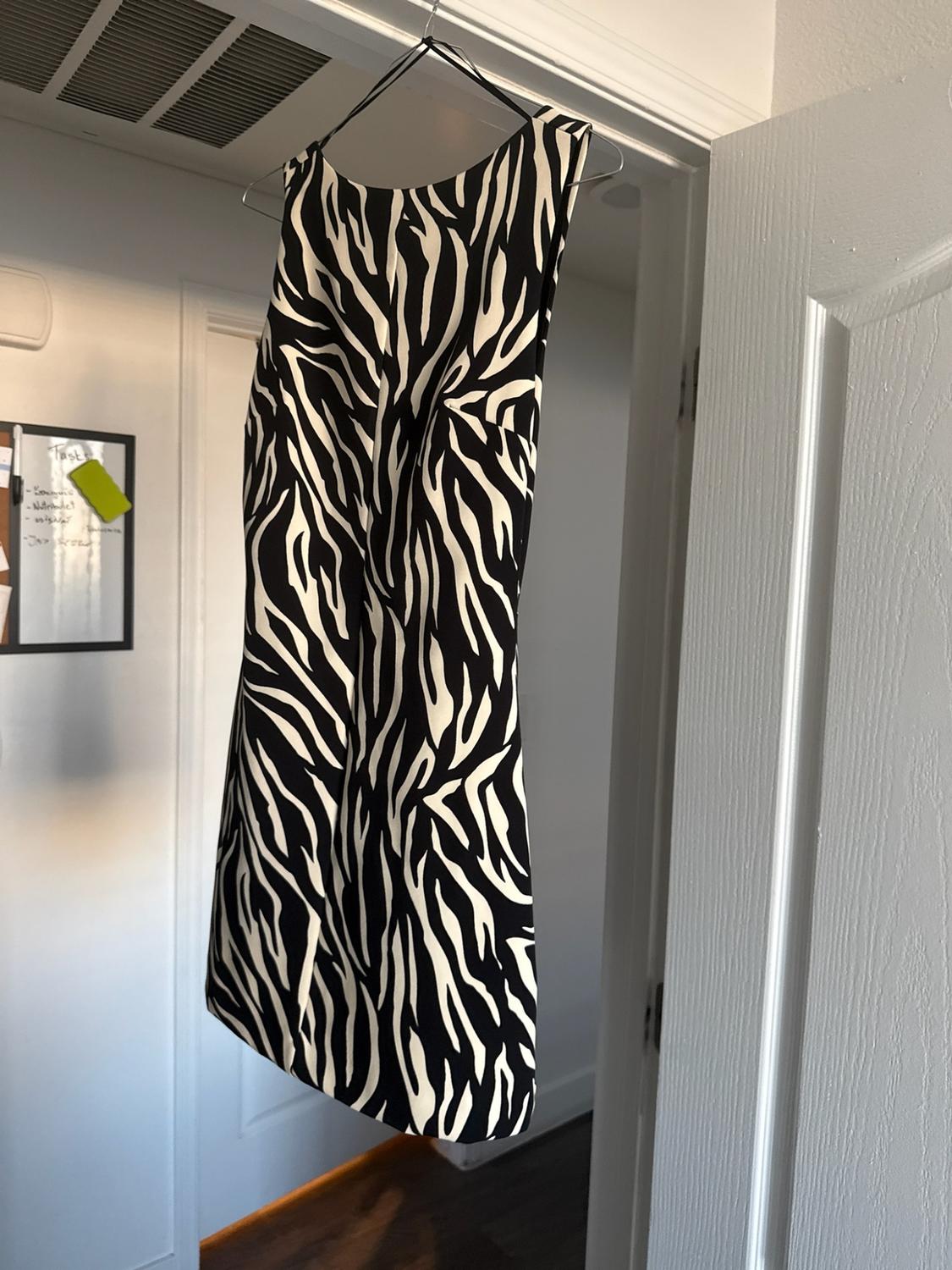 Sleeveless zebra-print dress hanging on a white door frame. In the background, a chalkboard with the text "Tasks."
