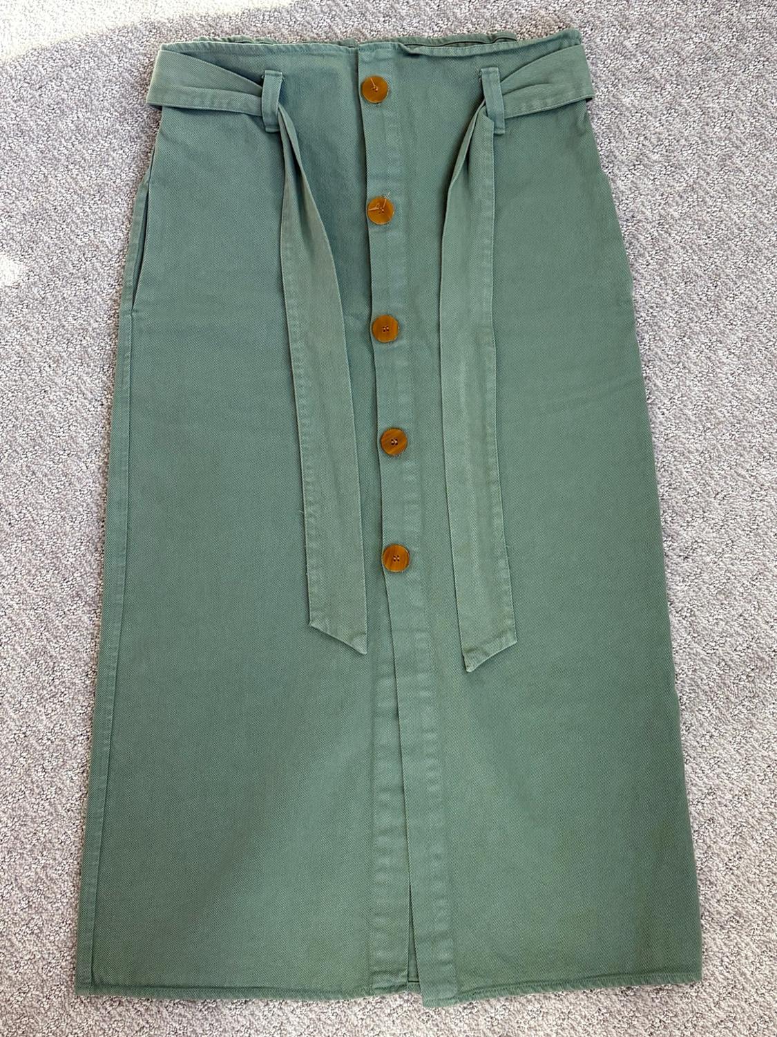 Green skirt with brown front buttons and a bow belt, laid out over a textured gray surface.