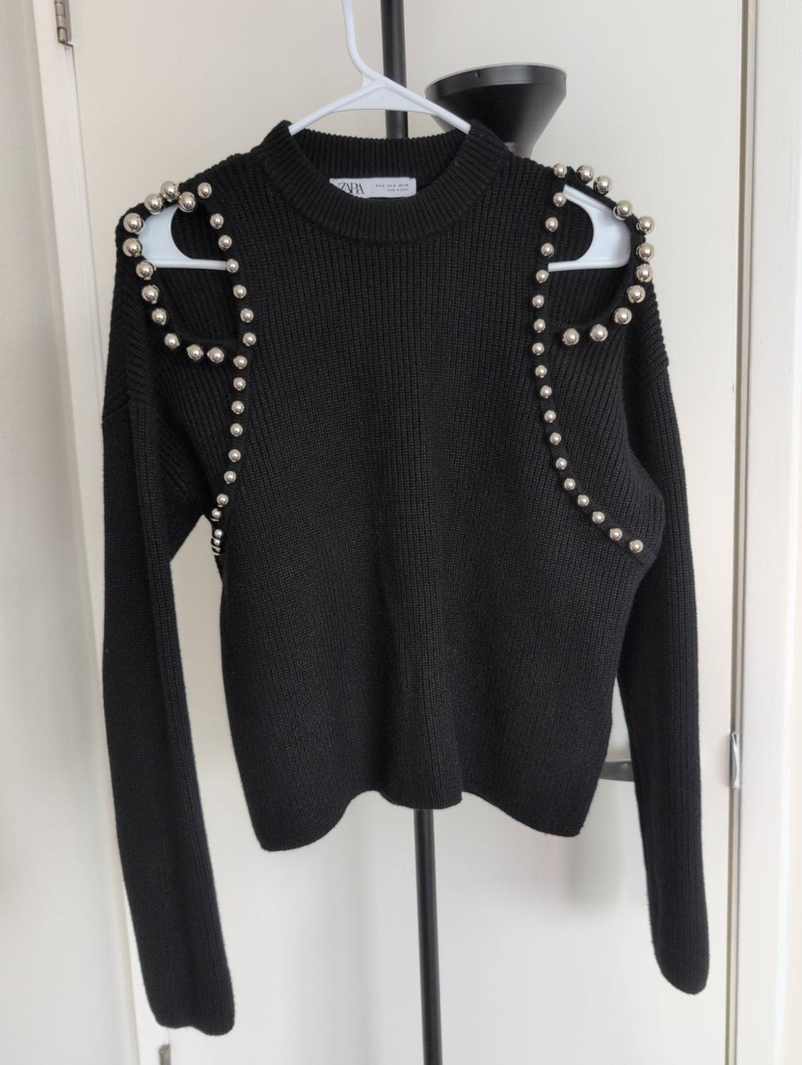 Black knit sweater with a round neck and long sleeves. Features shoulder cutouts decorated with silver studs. ZARA label.