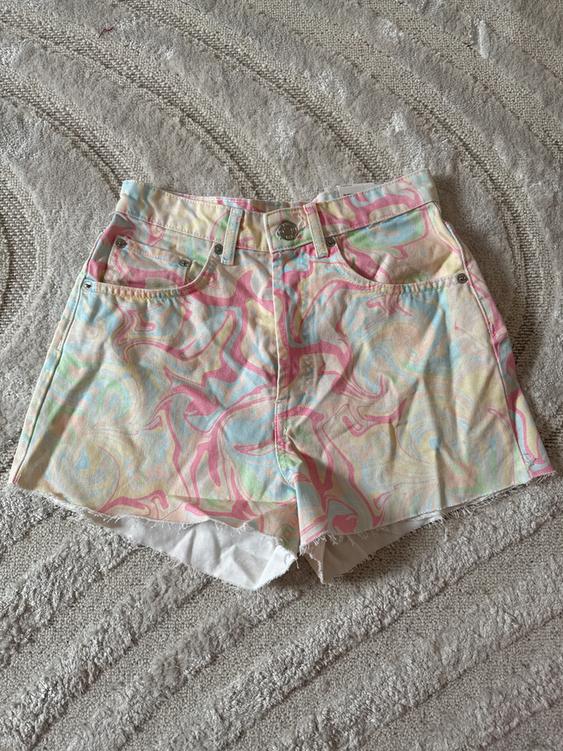 Denim shorts with a psychedelic print in pastel shades on a gray textured rug. Casual and summery design.