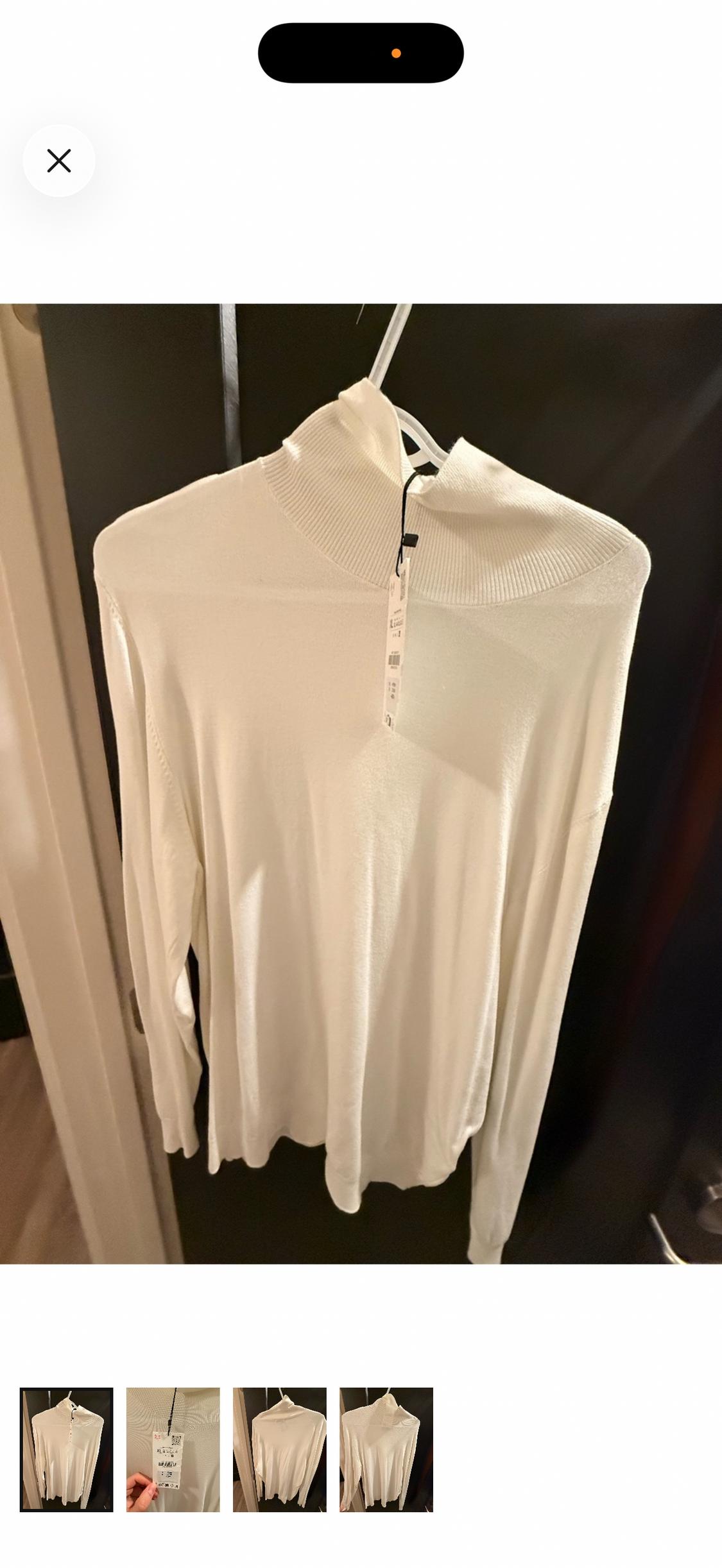 White long-sleeve, turtleneck sweater hanging on a white hanger in front of a dark door.