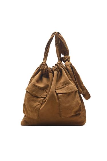 Brown fabric bag with drawstring closure, two front flap pockets and knotted handle, on a white background.