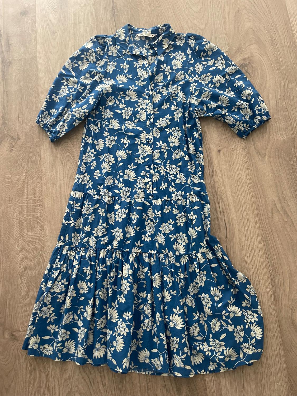 Blue dress with white floral print, three-quarter sleeves, and a shirt collar, on a light wood floor.
