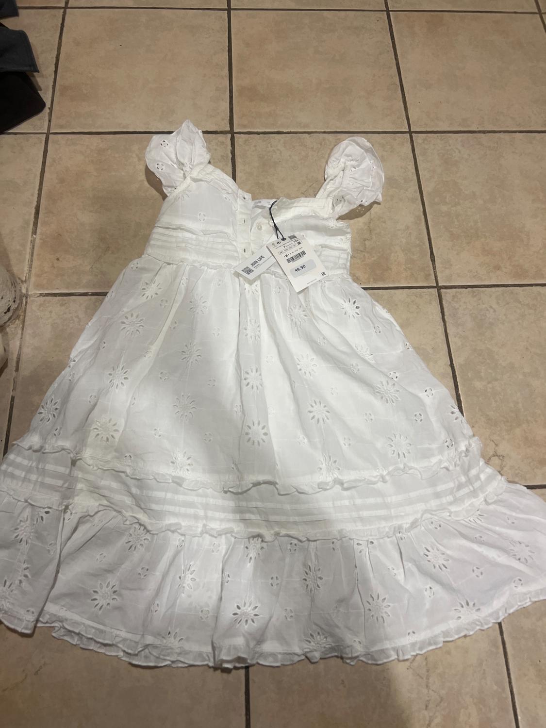 White lace dress with short puffed sleeves, laid on beige tiles. Price tags visible.