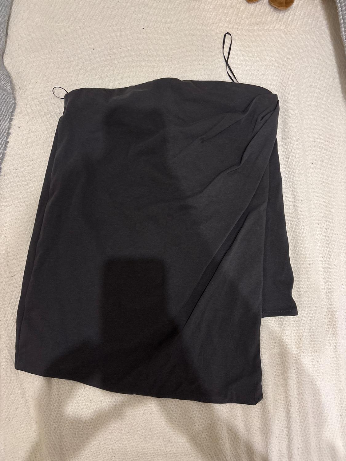 Black fabric folded over a light, textured surface. Two thin black strips are visible at the top.