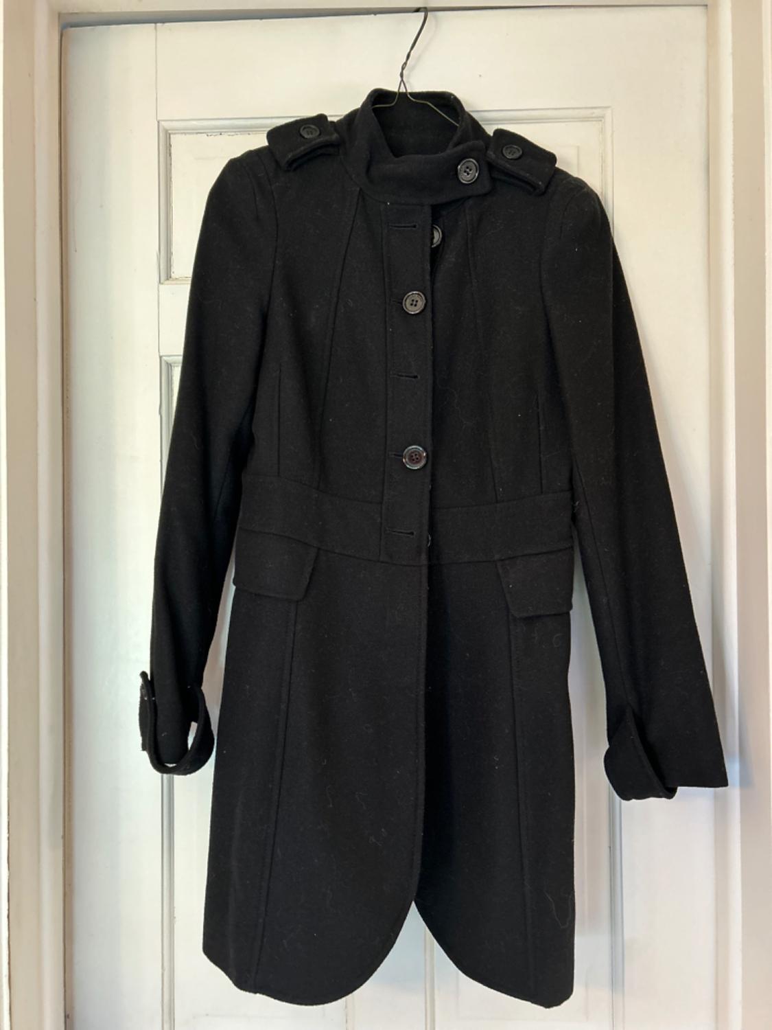 Front view of a black coat with a button fastening and flap pockets.