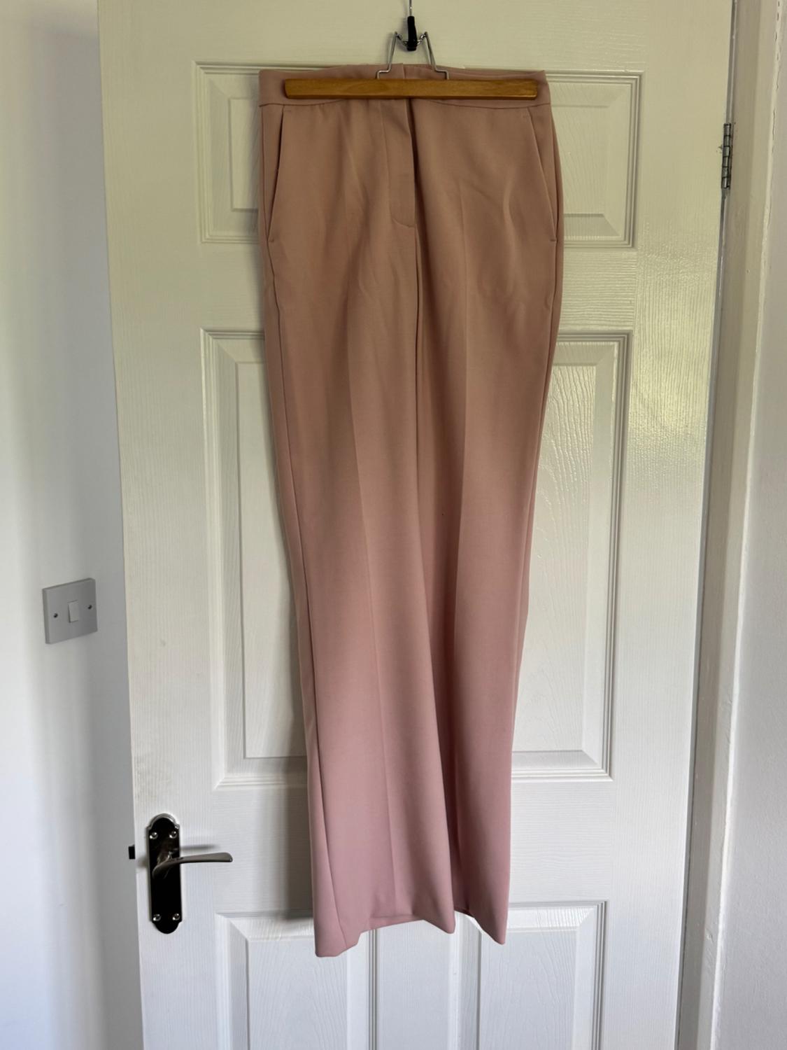 Light pink trousers hanging on a wooden coat hanger over a white door with a silver handle.